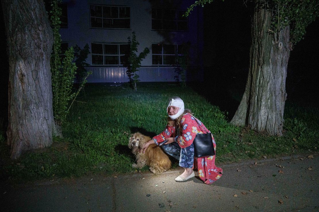 An injured woman sits with her dog near a house destroyed by a Russian airstrike.
